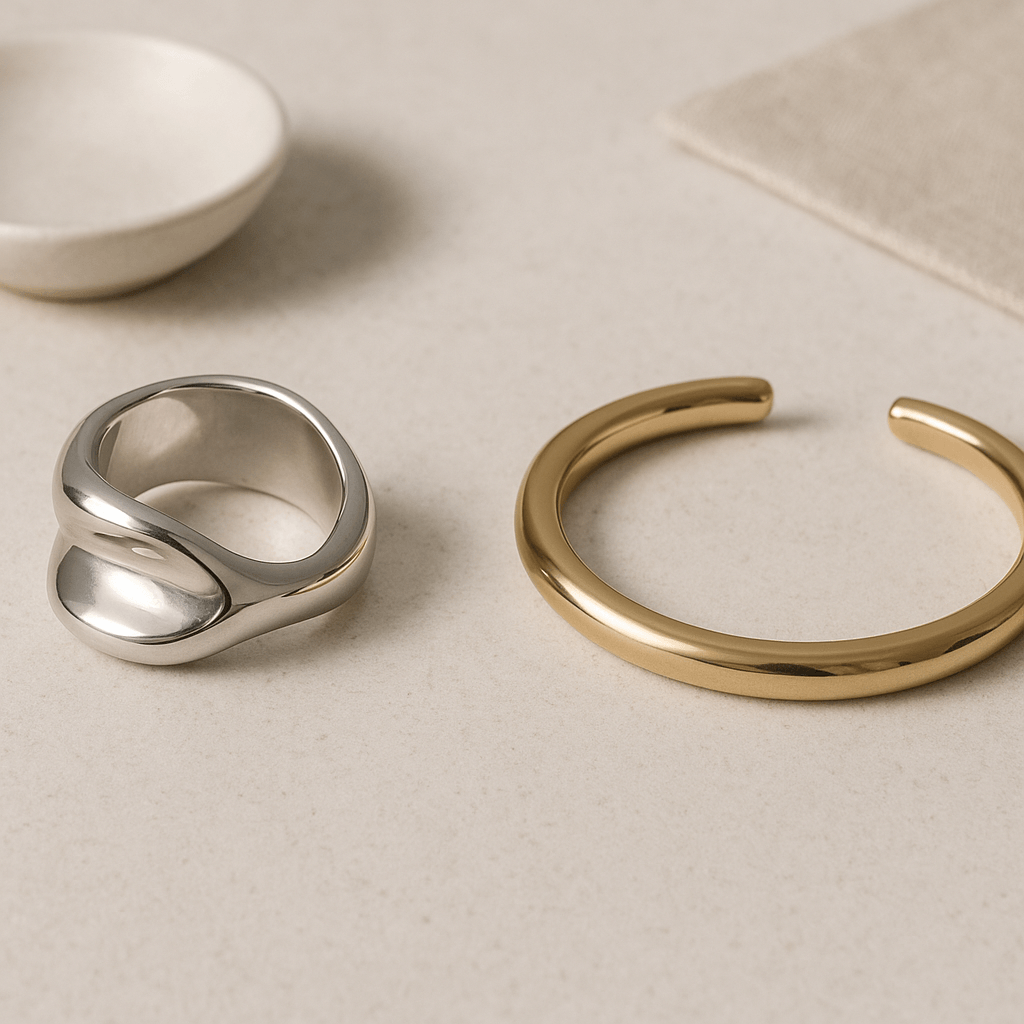 Deux bijoux contemporains disposés côte à côte sur une surface minérale claire.