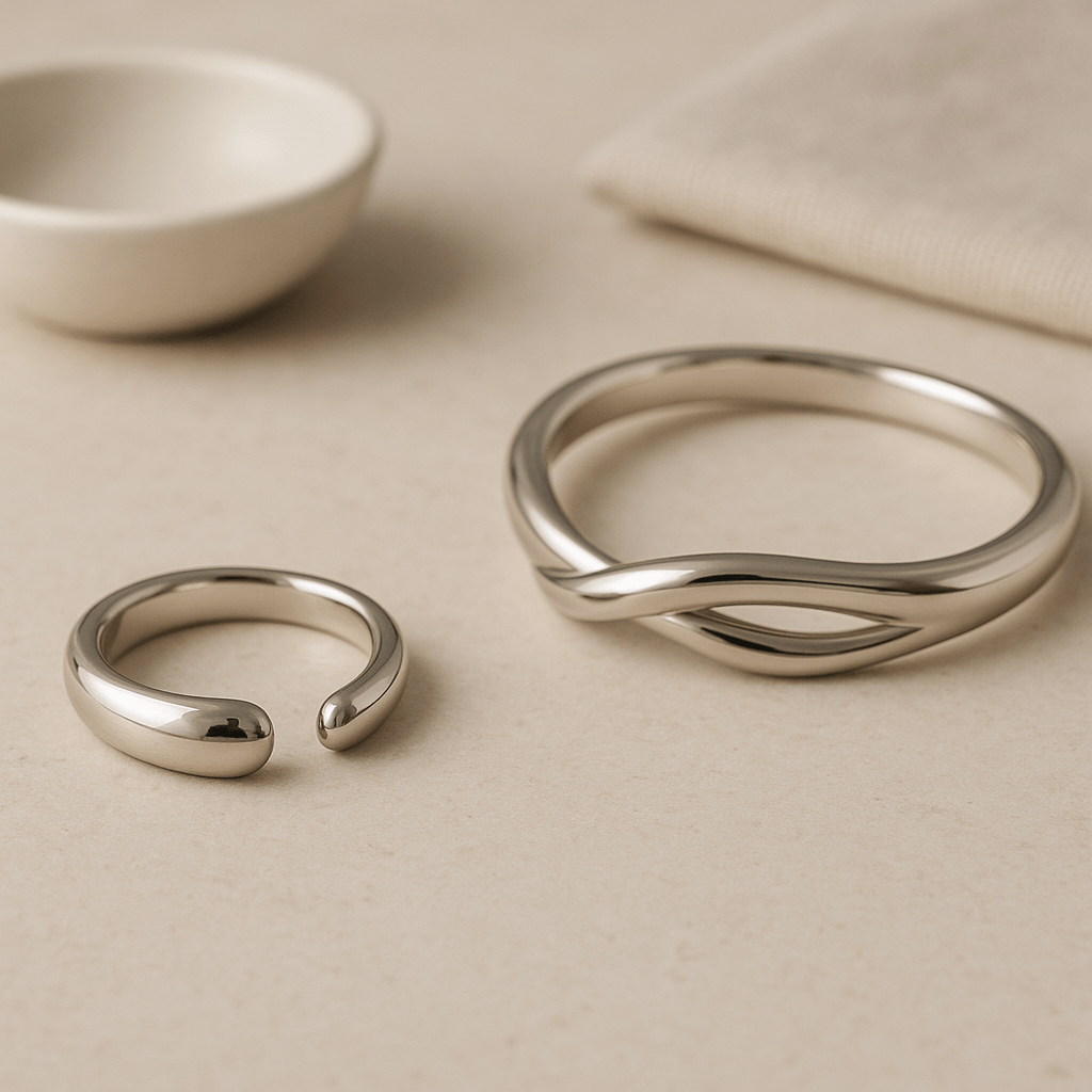 Deux bijoux génériques aux formes et finitions brillantes disposés sur une surface minérale claire.